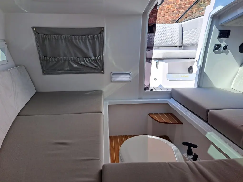 Interior of a boat featuring gray cushions, a wall pocket organizer, and a toilet, with a view of the outside seating area.